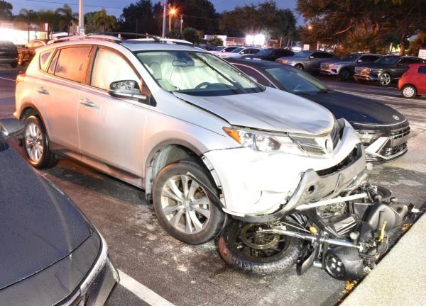 Gray car in parking lot with motorcycle underneath it