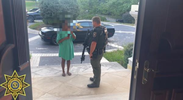 A member of the Fulton County Marshal's Department is seen speaking with one of the alleged squatters outside the Atlanta luxury home.