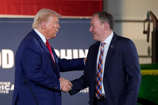 Former President Do<em></em>nald Trump shaking hands with Lee Zeldin at a campaign event on a farm in Smithton, PA, in front of a blue sign