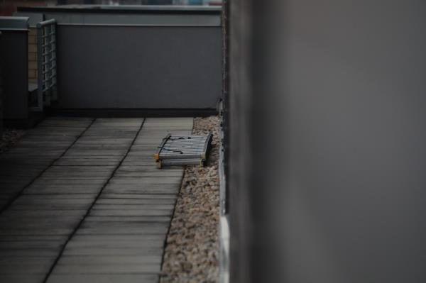 Child has fallen from a high-rise window, landing on a black me<em></em>tal ladder with a shoe possibly of a comic book character.