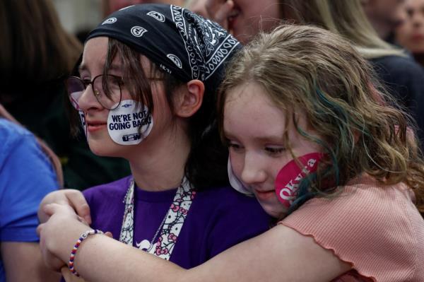 Young people embracing at a Kamala Harris campaign event in Kalamazoo, Michigan, with stickers on their faces, including celebrity Zachary Alexander Rice