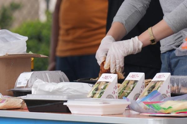 Sandwiches and food co<em></em>ntainers on an outdoor table with a pair of gloved hands in the background