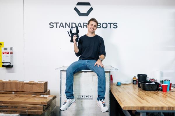 Founder and CEO of Standard Bots, Evan Beard, sitting on a box and holding a camera at their premises in Glen Cove, Long Island.