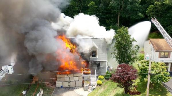 Firefighters from the Shelton Fire Department tackling a heavy fire in the garage of a cape-style house during a thunderstorm, with fireworks exploding inside the structure