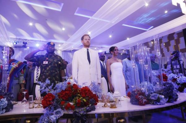 Prince Harry and Meghan, the Duke and Duchess of Sussex, at a charity reception in Abuja, Nigeria, standing in front of a group of people.