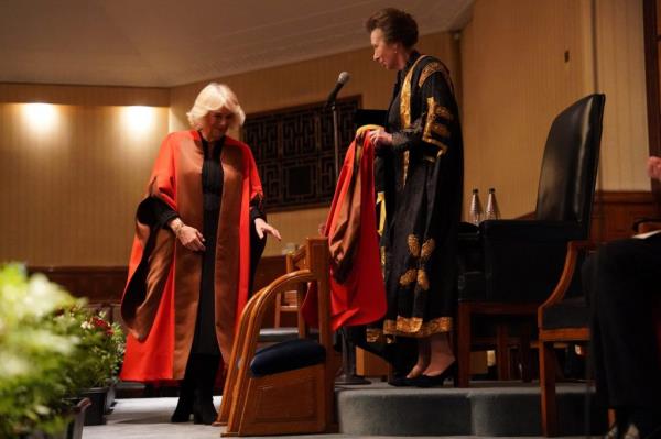 Britain's Queen Camilla walking in ceremo<em></em>nial attire after being awarded an Ho<em></em>norary Doctorate of Literature at the University of London, with Princess Anne looking on.