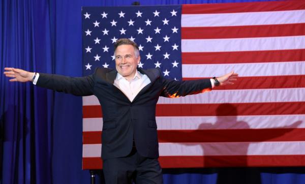 McCormick with arms out, US flag behind