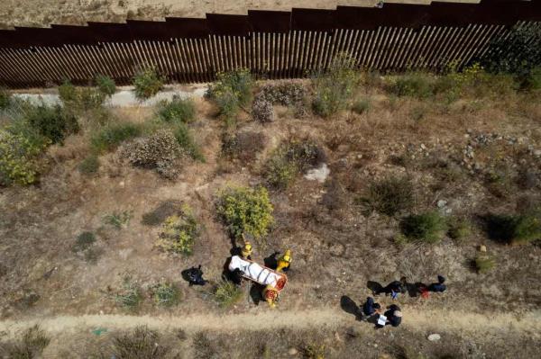 Aerial view of firefighters carrying the body of an alleged smuggler murdered near the US-Mexico border wall in Tijuana, Baja California state, Mexico, on June 15, 2022. 