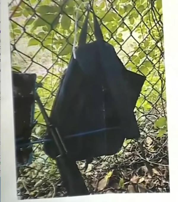 A backpack with Trump's image on it, hung on a fence, next to a gun
