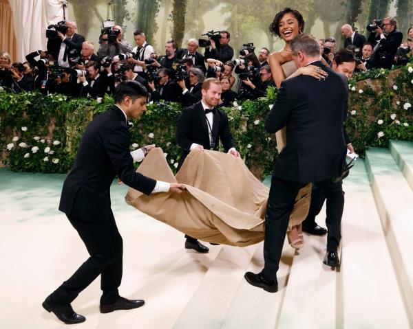 Tyla, the 'Water' singer, smiling as she's being carried up the Met Gala steps in a sculptural sand dress by a group of publicists, during the 2024 Costume Institute Benefit.