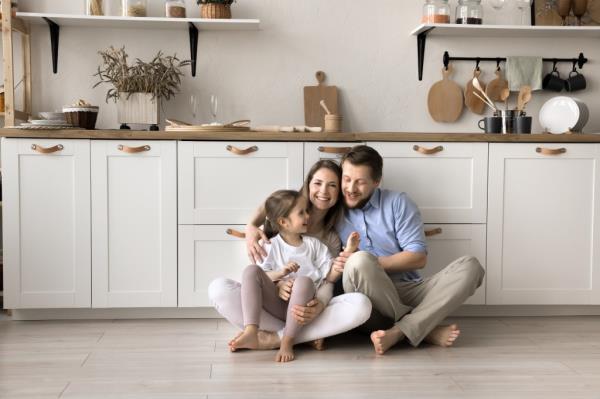 Family with daughter sit on floor in modern home kitchen.