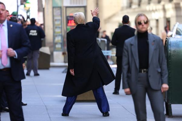 Former US President Do<em></em>nald Trump, in a long coat, waving while departing from a court hearing at 40 Wall Street, New York City.