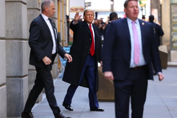 Former US President Do<em></em>nald Trump waving as he leaves 40 Wall Street in New York City after a news conference, wearing a business suit.