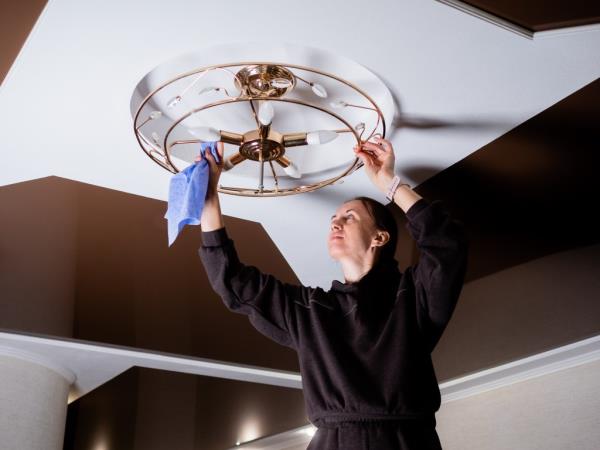 woman cleans the cobwebs and debris on the ceiling n