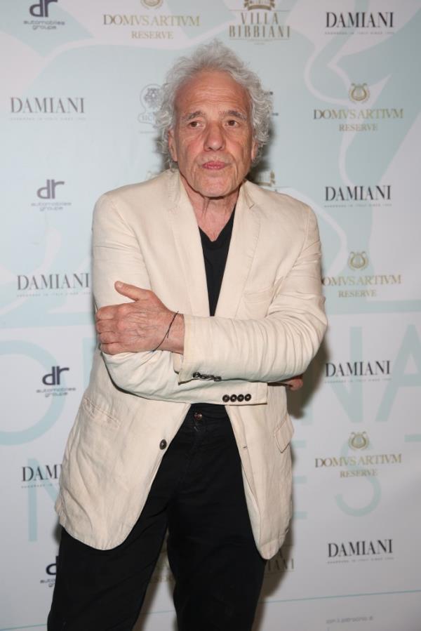 Director Abel Ferrara in a white blazer standing in front of a step and repeat.