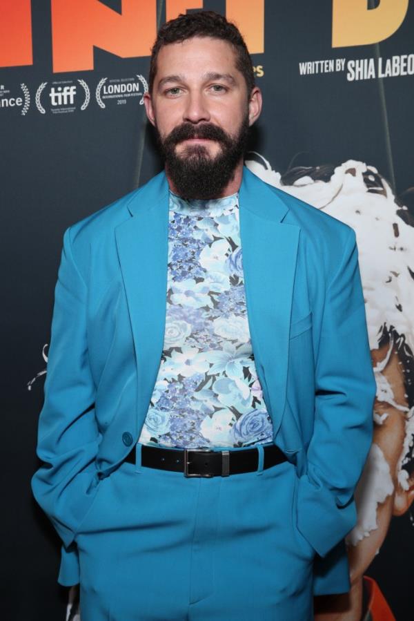 Shia LaBeouf in a blue suit and flora top poses on the red carpet in 2019.