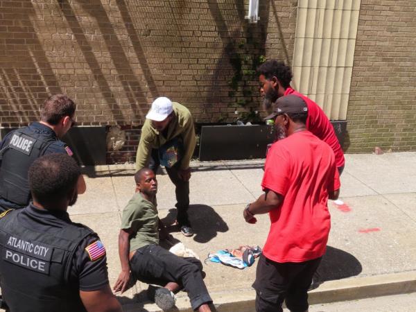 City outreach workers and police officers try to help a man sprawled on a sidewalk in Atlantic City, N.J., on Monday, July 1, 2024, the date city officials announced implementation of programs to address homelessness. (AP Photo/Wayne Parry)