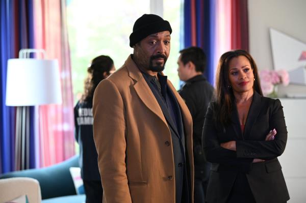 Jesse L. Martin and Maarha Hill as Alec and his estranged wife, Marisa. They're at a crime scene looking off-camera. Jesse is wearing a black winter cap and a tan overcoat and Maarha has her arms crossed and is smiling very slightly.