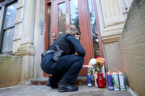 A cop places a candle next to the door leading to Jackie Billini's apartment. 
