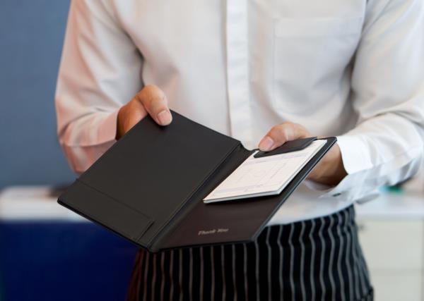 A waiter in a white shirt and apron presenting a receipt