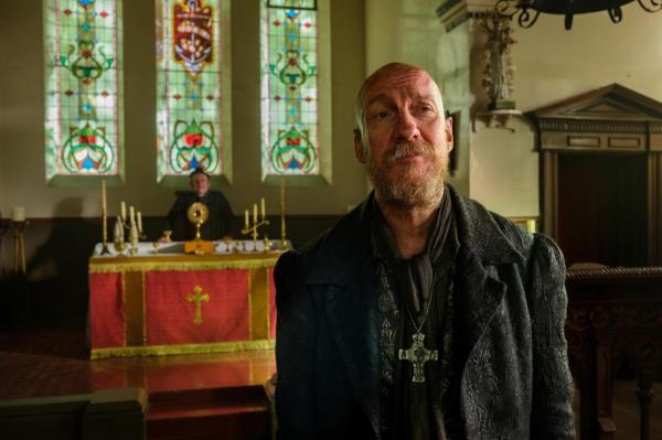 David Thewlis smirking, bald with a beard. 
