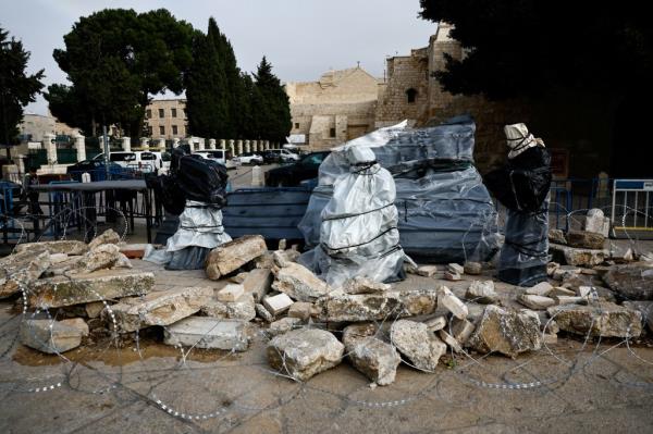 A Christmas installation of a grotto with covered figures standing amid rubble surrounded by a razor wire, is displayed outside the Church of the Nativity
