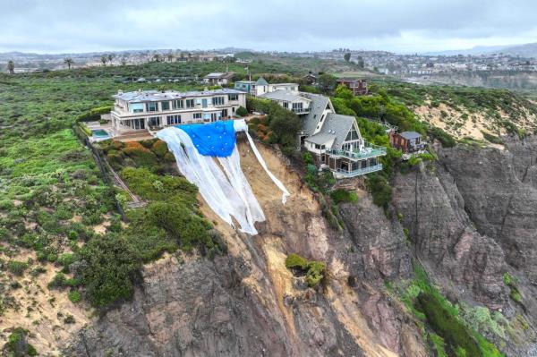 Tarps hang behind a cliff-top home above a landslide along Scenic Drive in Dana Point, Calif., on Feb. 20, 2024.