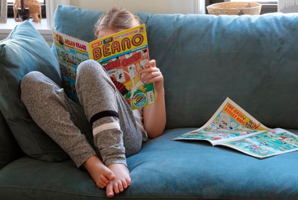 A girl reads a book on a couch.