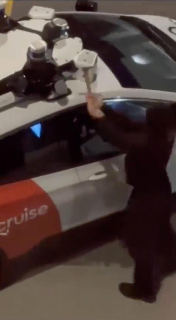 A masked man wearing a black hoodie was filmed bashing a Cruise robotaxi with a hammer.