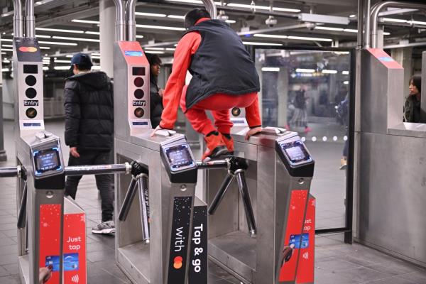 a man in a red track suit red sneakers and black vest and hat jumping the turnstile at a subway station in NYC