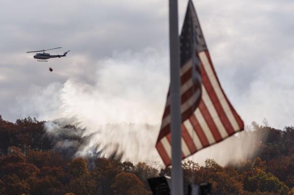 US flag at half-staff, a Maine Forest Service helicopter releasing water on a raging wildfire on Lamentation Mountain, Berlin, Connecticut, USA