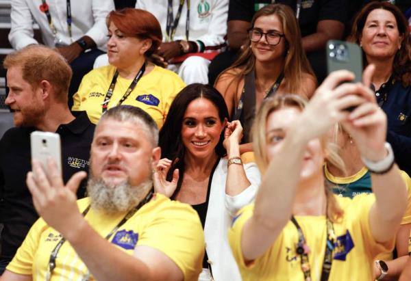Spectators take selfies with Britain's Meghan (C), Duchess of Sussex and Britain's Prince Harry (L), Duke of Sussex, as they watch a wheelchair basketball competition at the 2023 Invictus Games in Duesseldorf, western Germany on September 13, 2023.