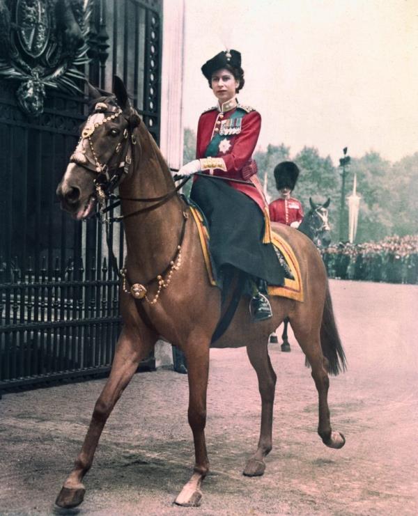 Princess Elizabeth in a red uniform riding a horse during a trooping ceremony