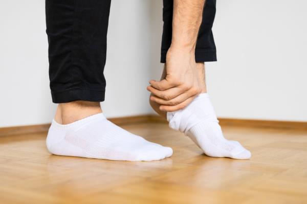 human feet putting on white ankle socks by hand standing on wooden floor.