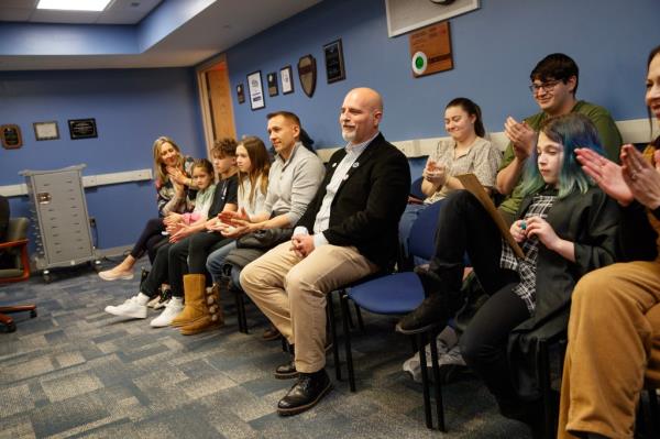 Teacher Joseph Nappi sits in a room with other children and adults. 