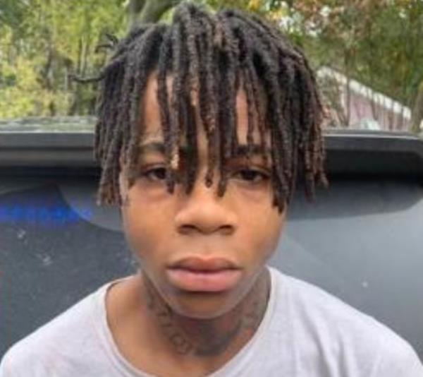 A young man with short dreads, a white t-shirt and visible neck tattoos stands facing the camera.