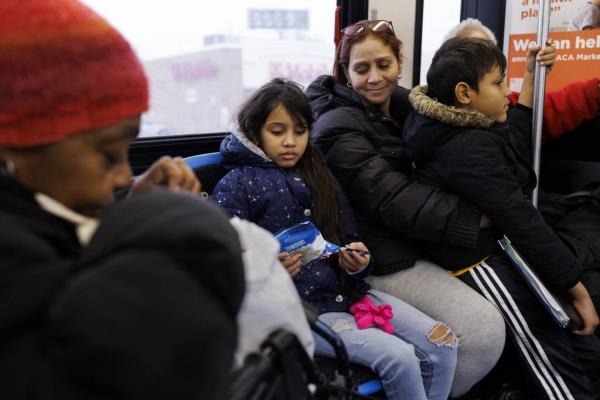 Yuledy, center, looks at a bag of chips given to her by a woman, left, as she rides a CTA bus with her brother Pedro and their mother Esperanza while traveling from their home in Englewood to Stroger Hospital on Nov. 21, 2023, in Chicago. 