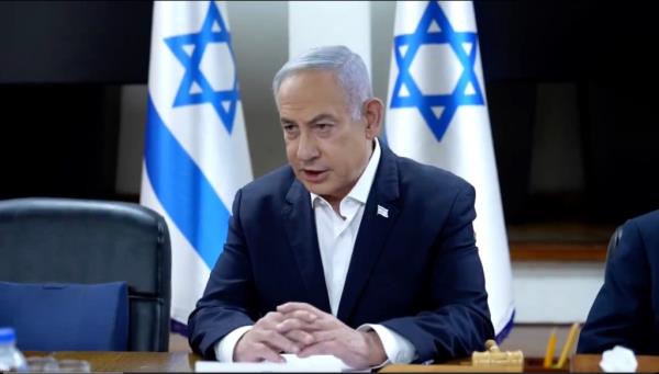 Prime Minister Benjamin Netanyahu sitting at a desk with flags behind him, during a War Cabinet meeting at the Kirya in Tel Aviv