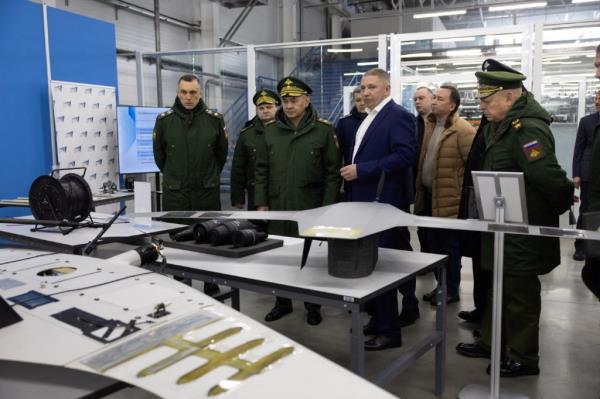 Russian Defence Minister Sergei Shoigu and nine other officials look at dro<em></em>nes on tables at a factory producing the unmanned weapons.