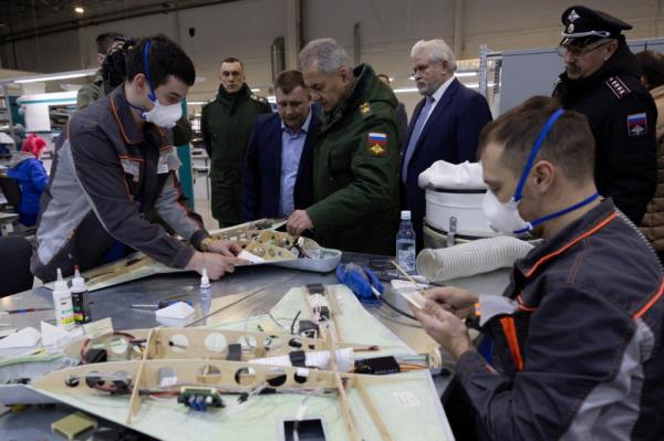 Russian Defence Minister Sergei Shoigu surrounded by officials and workers wearing masks while inspecting a drone factory.