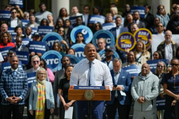 Mayor Eric Adams speaking at a podium at a budget rally with advocates for working-class New Yorkers on City Hall steps