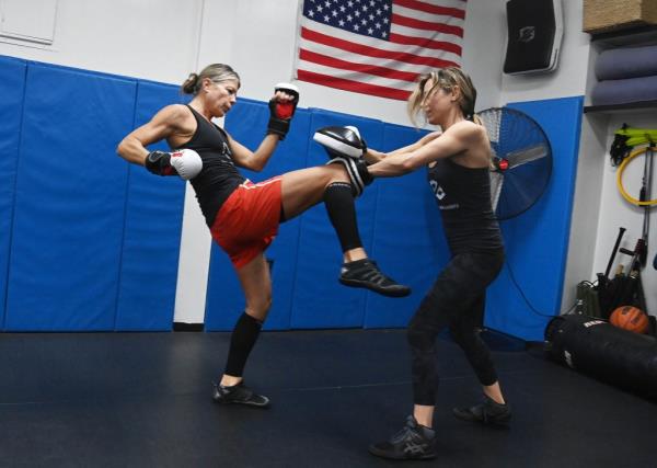 One woman knees a pad in another woman's hands as part of a self-defense class.