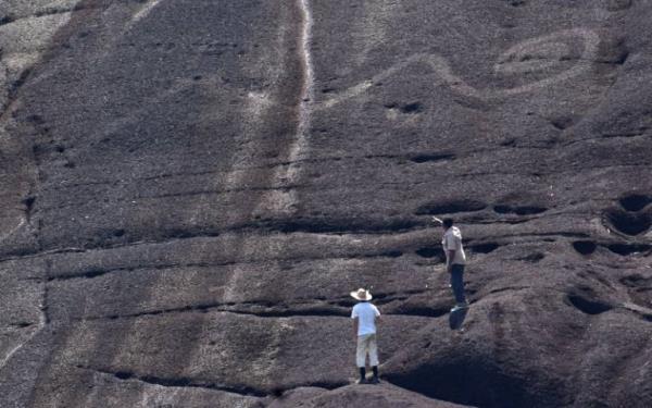 Two researchers inspect the large etchings on the side of a rocky cliff.