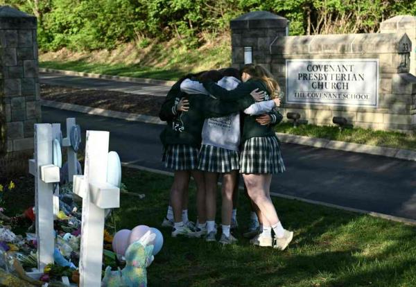 Girls embrace in front of a makeshift memorial for victims by the Covenant School building at the Covenant Presbyterian Church following a shooting, in Nashville, Tennessee, March 29, 2023.