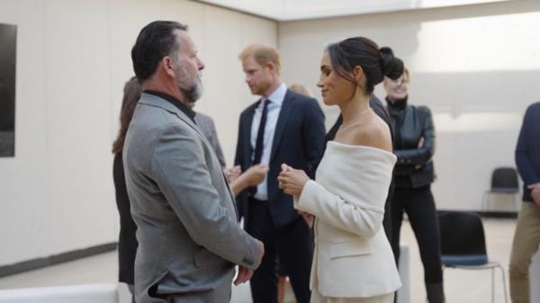 Meghan, Duchess of Sussex in a suit, standing in front of a microphone speaking.