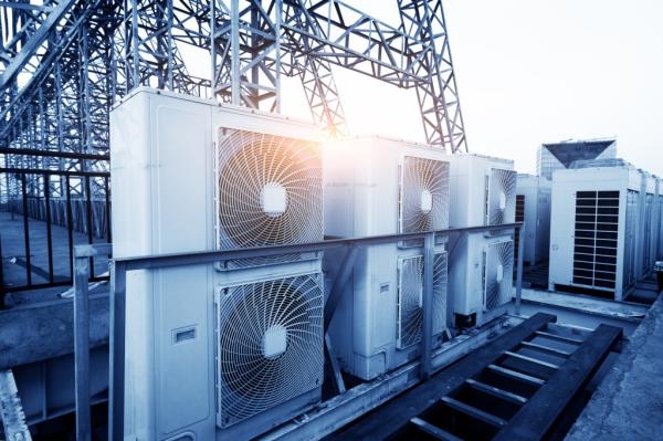 Air co<em></em>nditioner units (HVAC) on a roof of industrial building with blue sky and clouds in the background.