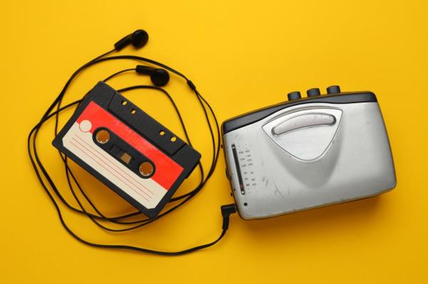 Silver cassette tape recorder and headpho<em></em>nes on a yellow surface, signifying nostalgia and simplicity of music in past times