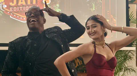 Sooni Tarapore<em></em>vala Archie Burnett and Mekhola Bose smile and mirror each other's poses: right arm on the hip, left arm with elbow out and the hand on the head 