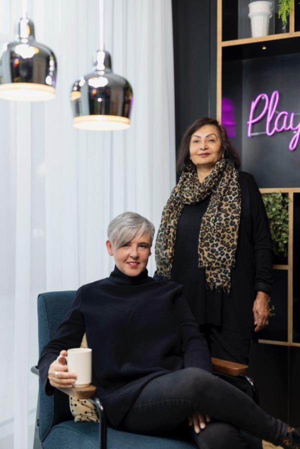 Ruth Sparkes sitting on a blue chair with her SaferSpace.io business partner, Sunita, standing next to her.